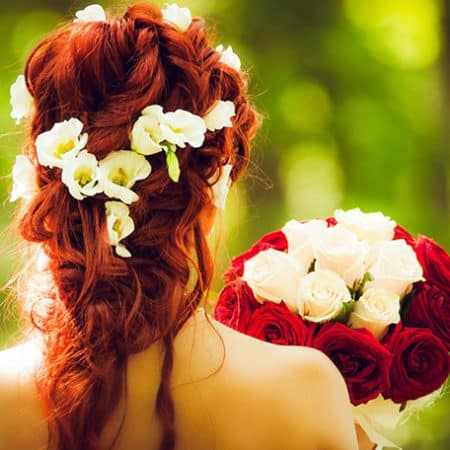Na zdjęciu widoczna Panna Młoda w upięciu ślubnym. Włosy koloru rudego z wplecionymi żywymi kwiatami eustemii w kolorze białym. Kadr portretowy tyłem.