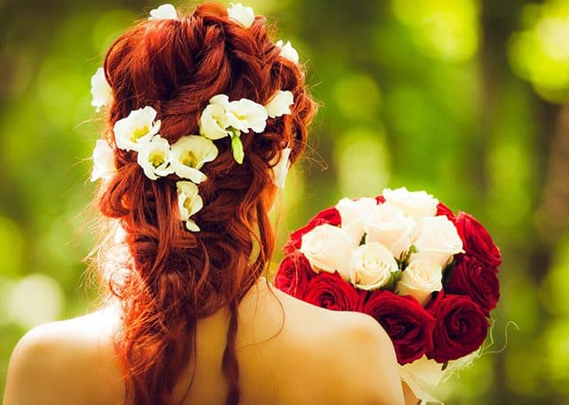 Na zdjęciu widoczna Panna Młoda w upięciu ślubnym. Włosy koloru rudego z wplecionymi żywymi kwiatami eustemii w kolorze białym. Kadr portretowy tyłem.