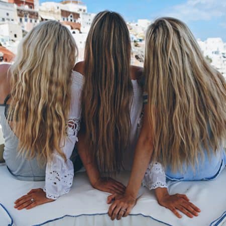 Na zdjęciu widoczne są 3 kobiety z długimi, rozpuszczonymi, lekko falowanymi włosami koloru blond, pozujące na tle wakacyjnego widoku. Kadr tyłem w ujęciu amerykańskim.