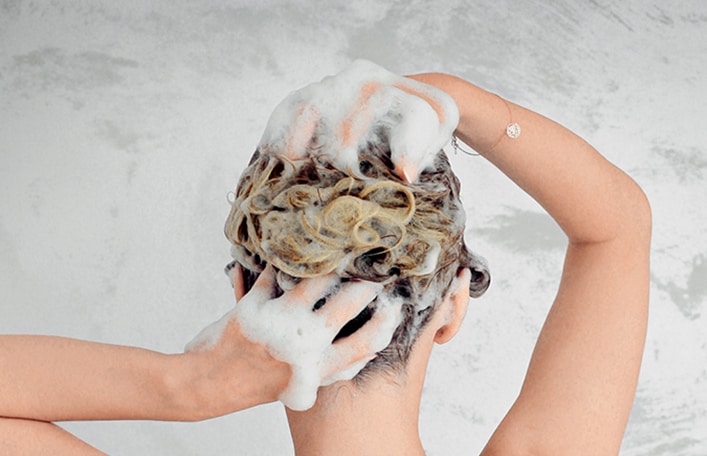 Na zdjęciu widoczna jest sylwetka kobiety sfotografowana tyłem podczas zabiegu mycia głowy pod prysznicem. 