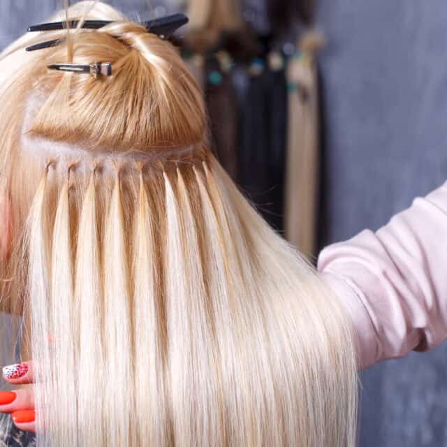 Na zdjęciu widoczny jest tył kobiecej głowy podczas zabiegu przedłużania włosów metodą keratynową.