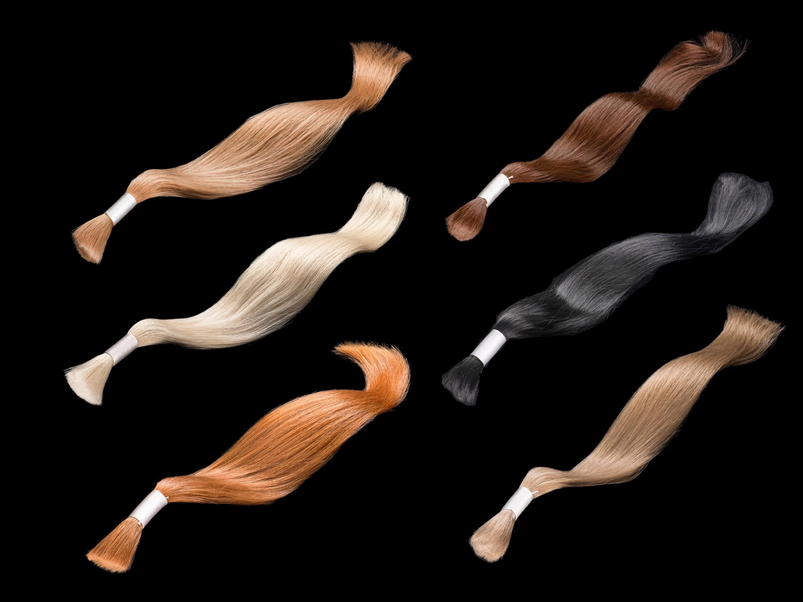 Zdjęcie przedstawia kolorowe pasma włosów do doczepienia na czarnym tle. 