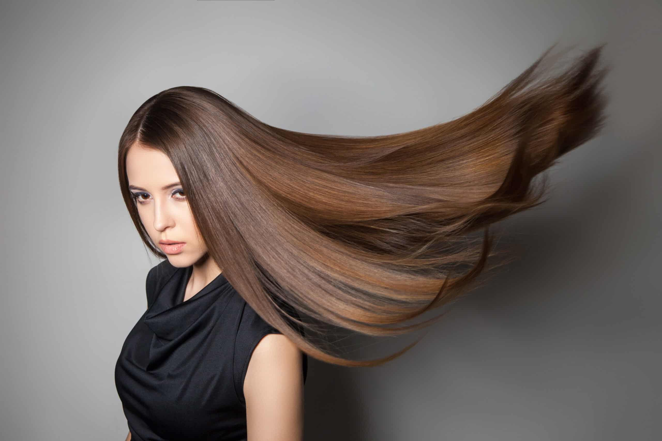 Na zdjęciu widoczna jest młoda kobieta, która ma długie brązowe włosy, które są rozwiane przez wiatr. 
