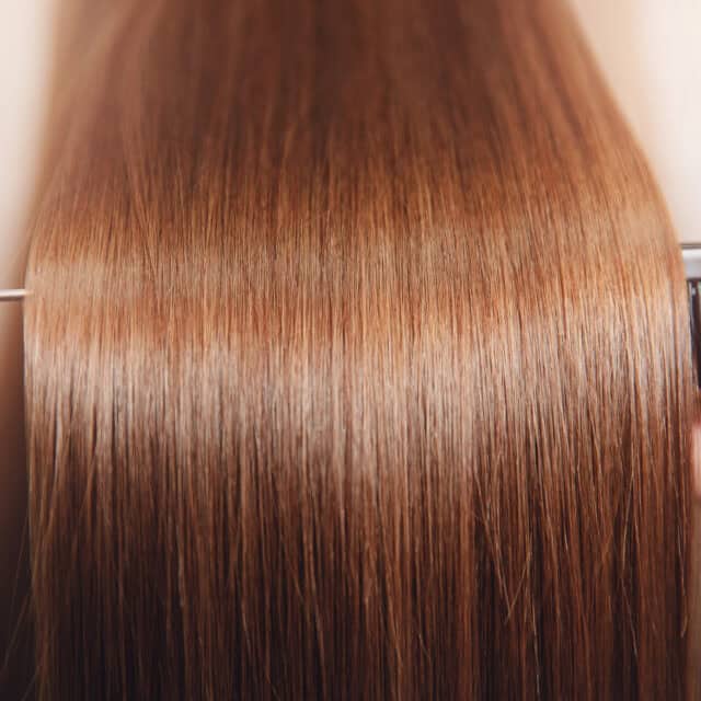 Zdjęcie przedstawia długie proste lśniące włosy o kolorze jasnego brązu.